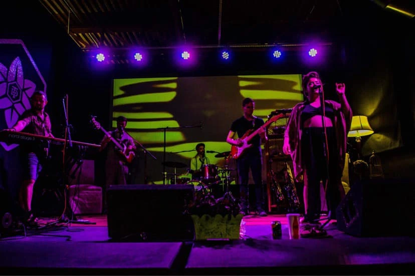 A band playing on a stage with a psychedelic background and purple lights.
