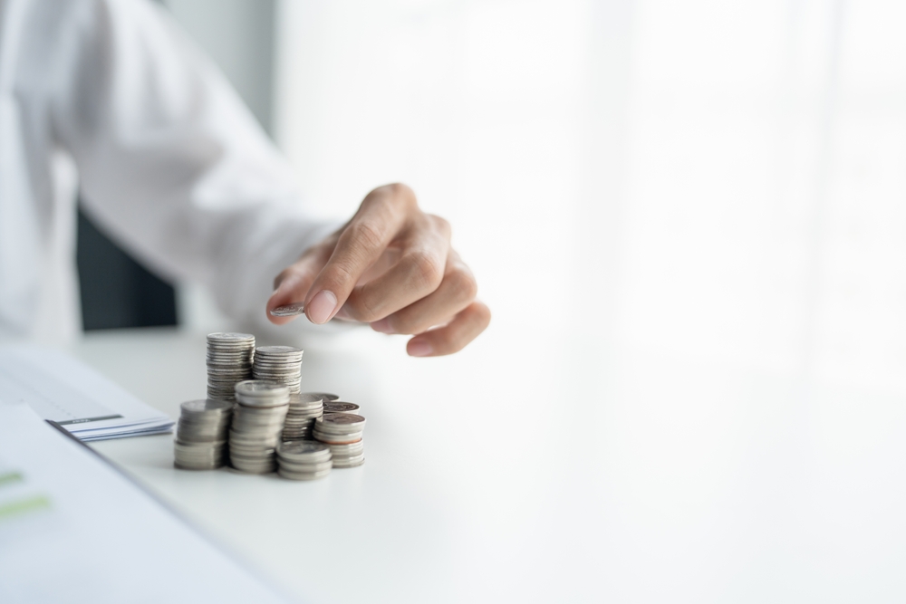 Person stacking coins on a white surface near paperwork.