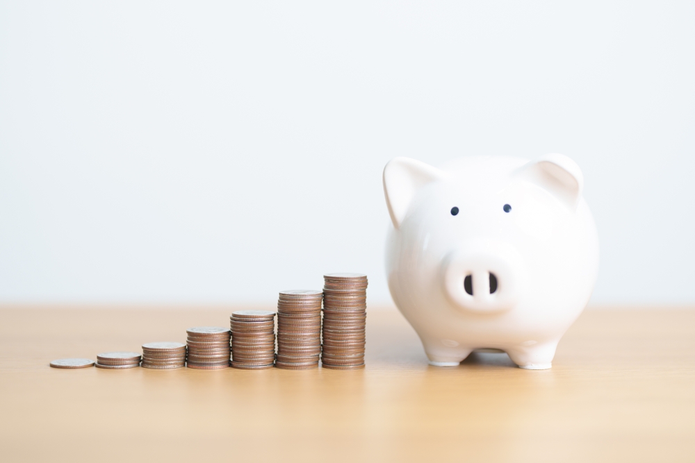 White piggy bank next to stacks of coins arranged in ascending order on a wooden surface.