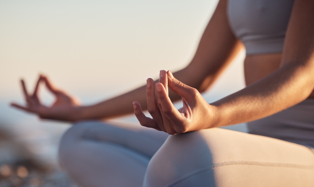 Person sitting cross-legged outdoors practicing meditation with hands in a mudra position.
