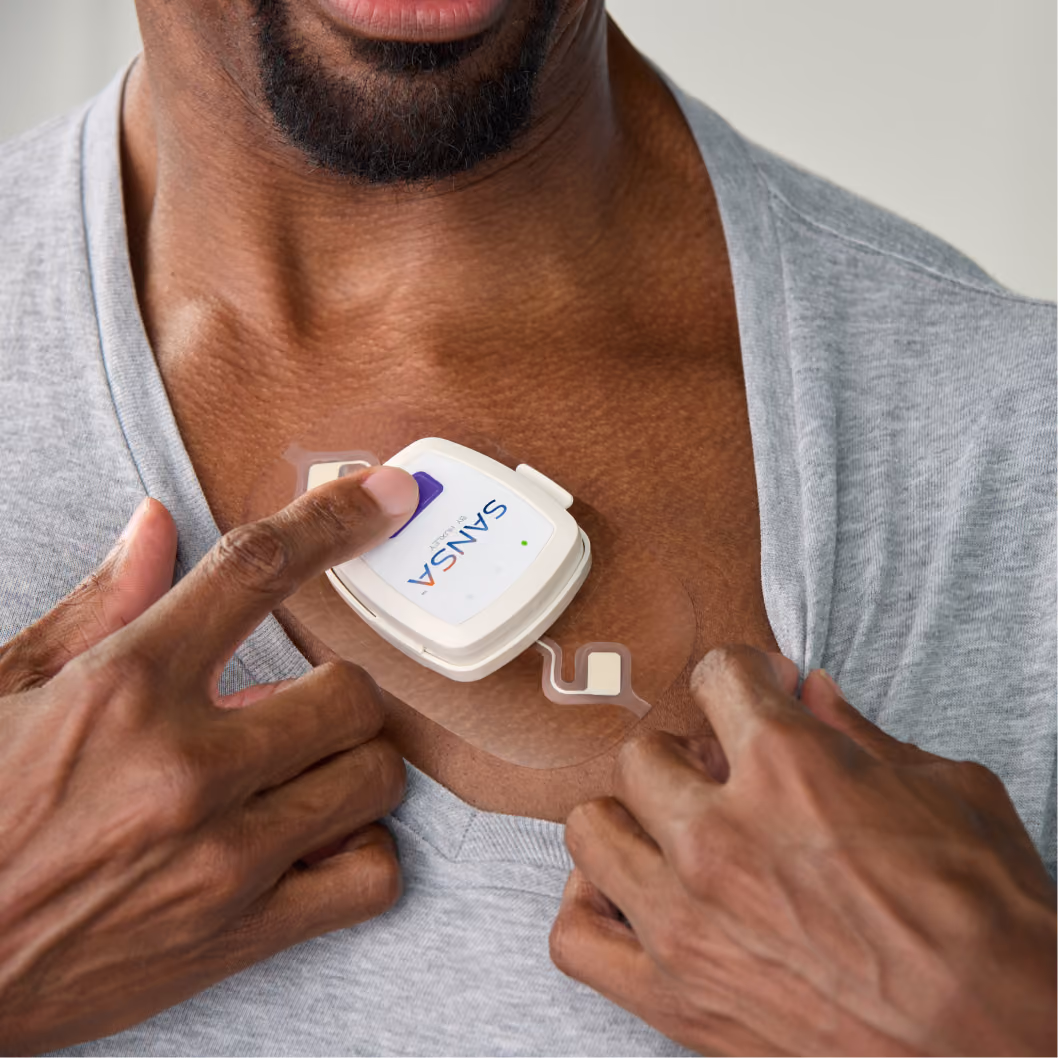 Man pressing the SANSA device button while wearing the patch on his chest