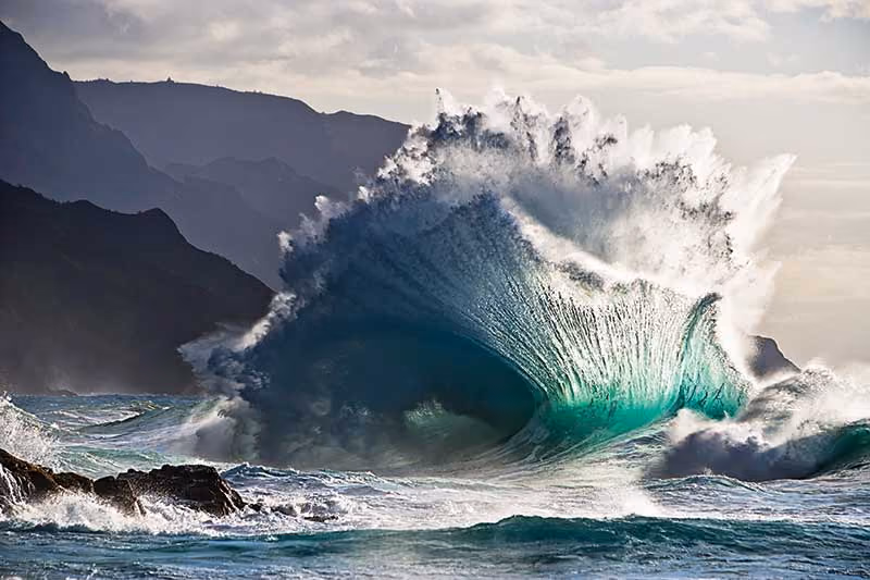 A large wave of ocean water rising just before it crashes to the rocky shoreline.