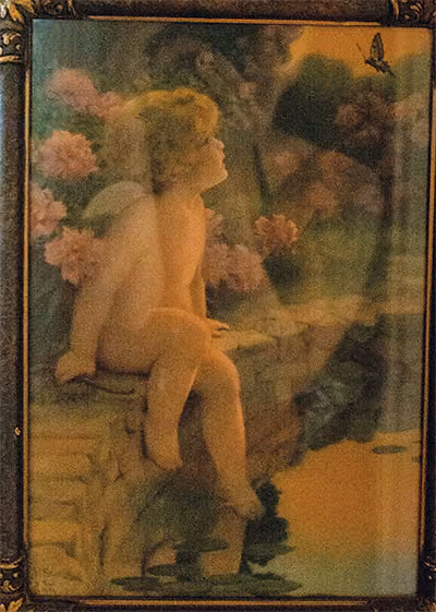 A painting of a small child with wings sitting on a stone bridge near a bunch of pink flowers.
