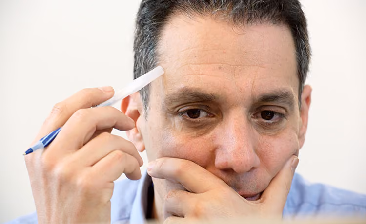 Hany Farid holds a pen in his right hand and covers mouth with his left deep in thought.