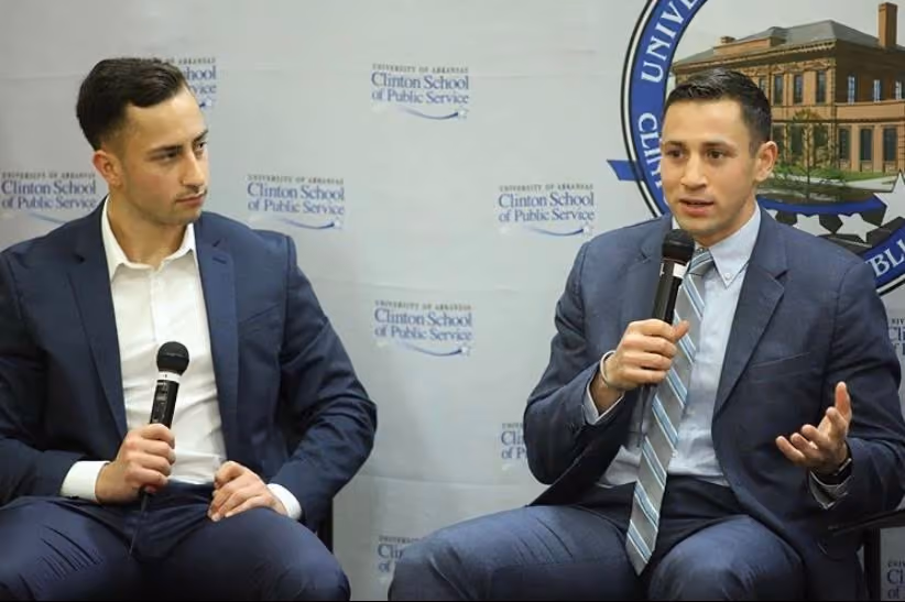 The Fiorito seated and holding microphones in front of a banner that reads "University of Arkansas Clinton School of Public Service"