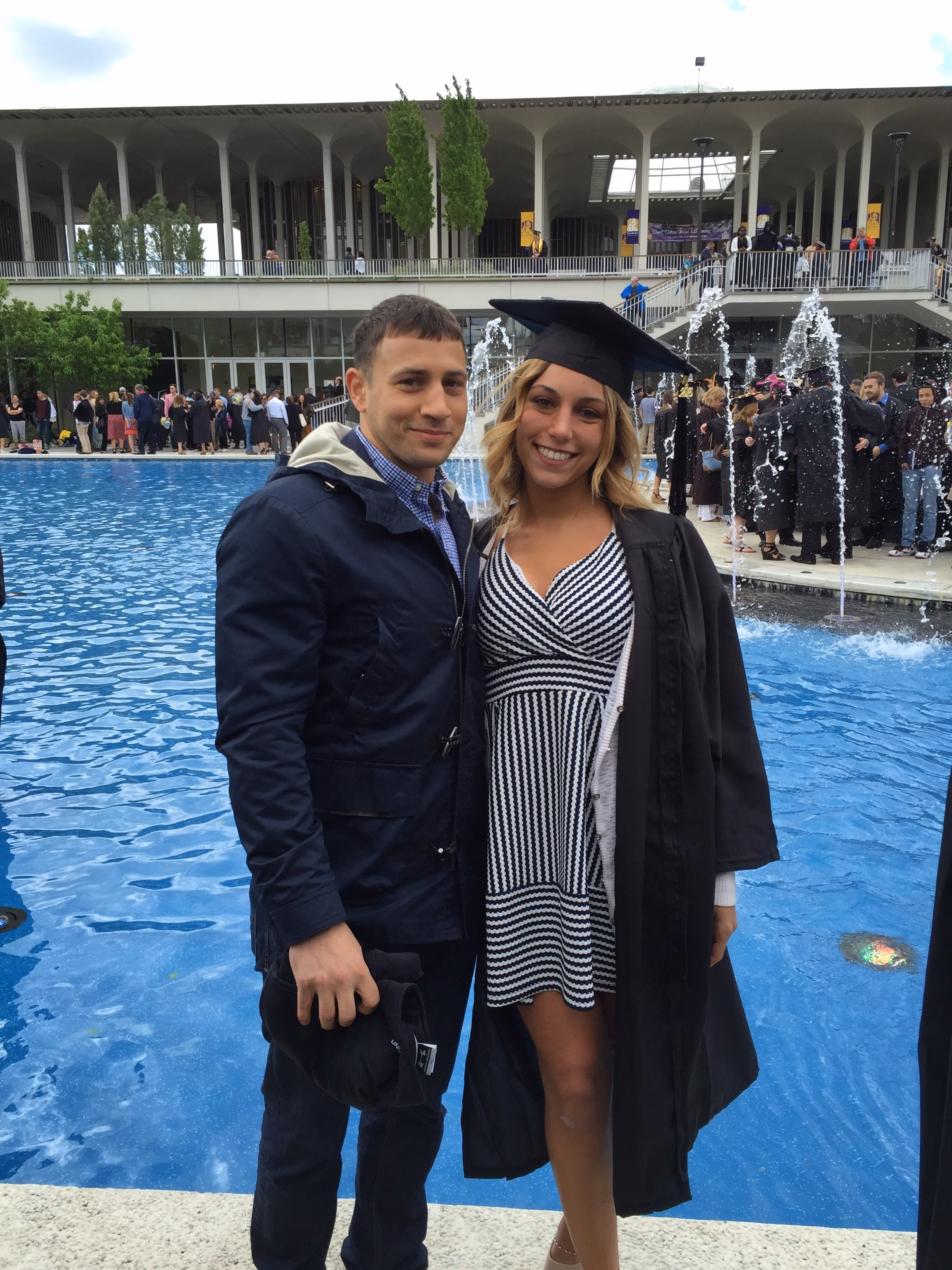 Nick Fiorito stands with a young woman dressed in graduation cap and gown on the campus of the University at Albany.
