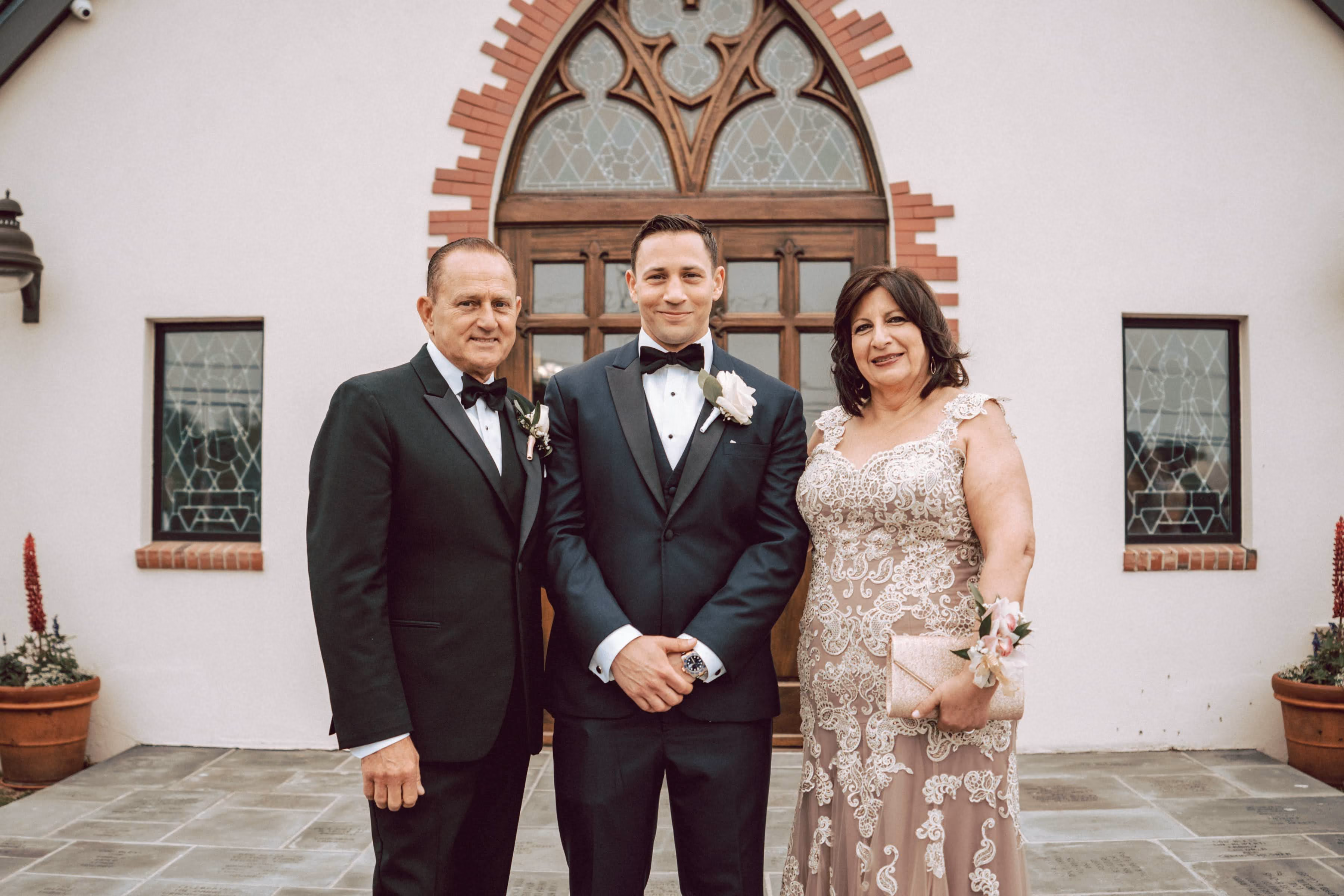 Nick Fiorito, dressed in a tuxedo, stands with his parents flanking him on both sides on his wedding day.