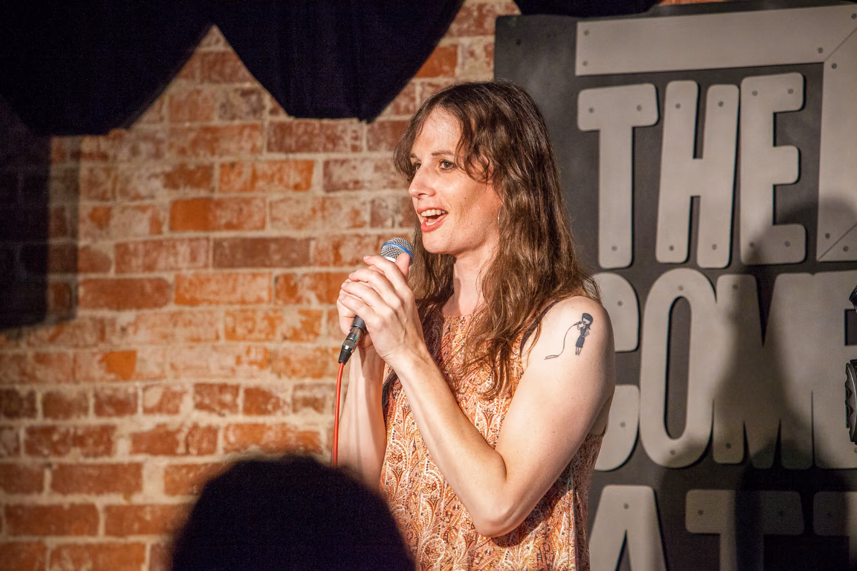 Comedian Jaye McBride, a transgender woman, stands on stage holding a microphone while performing a comedy routine.