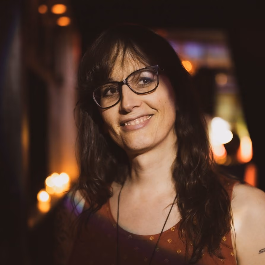 A portrait shot of Jaye McBride, a white transgender woman with shoulder-length hair,earing glasses.