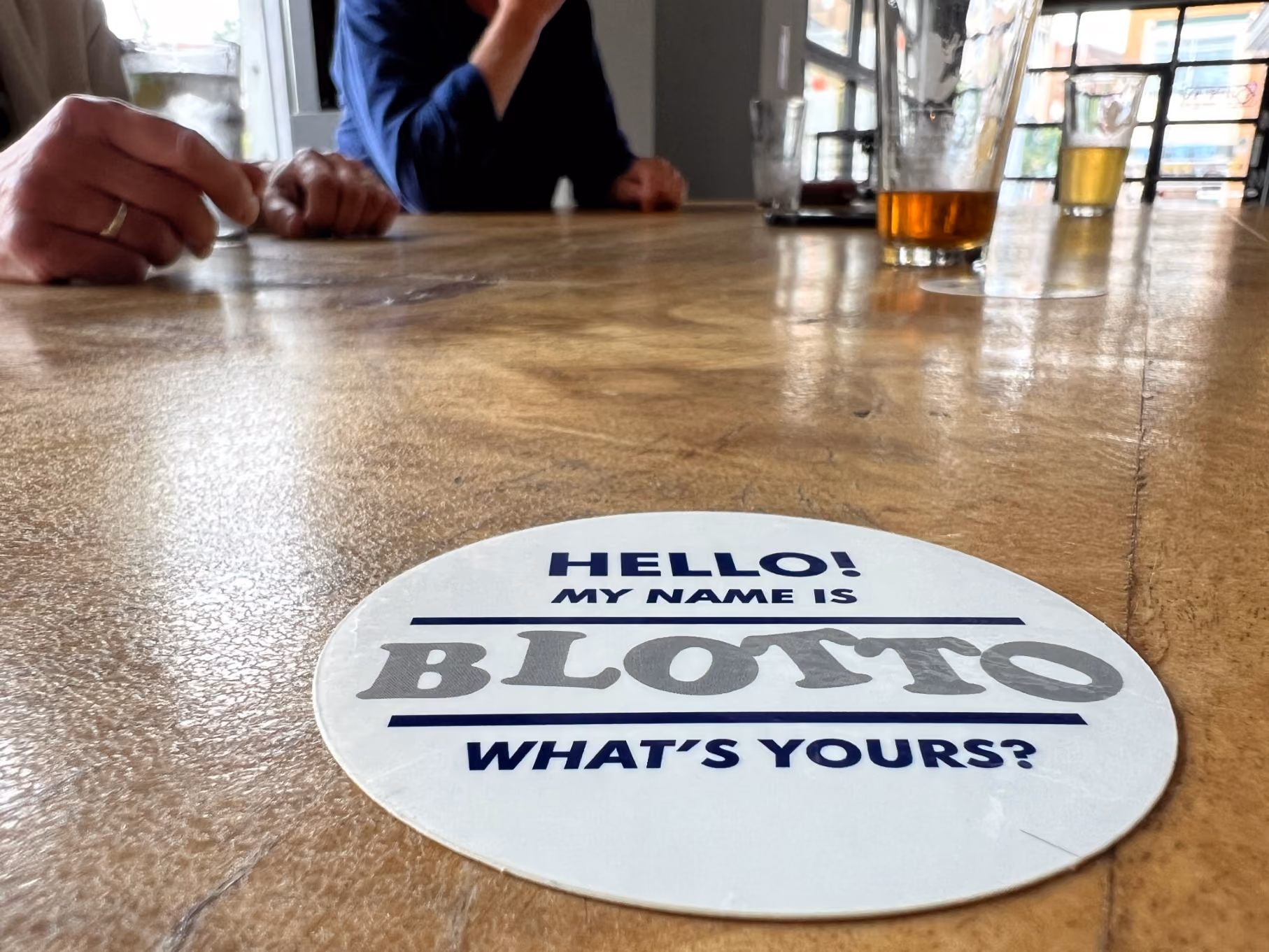 Close-up of a round sticker on a table with Blotto's signature catchphrase: "Hello! My name is Blotto. What's Yours?"
