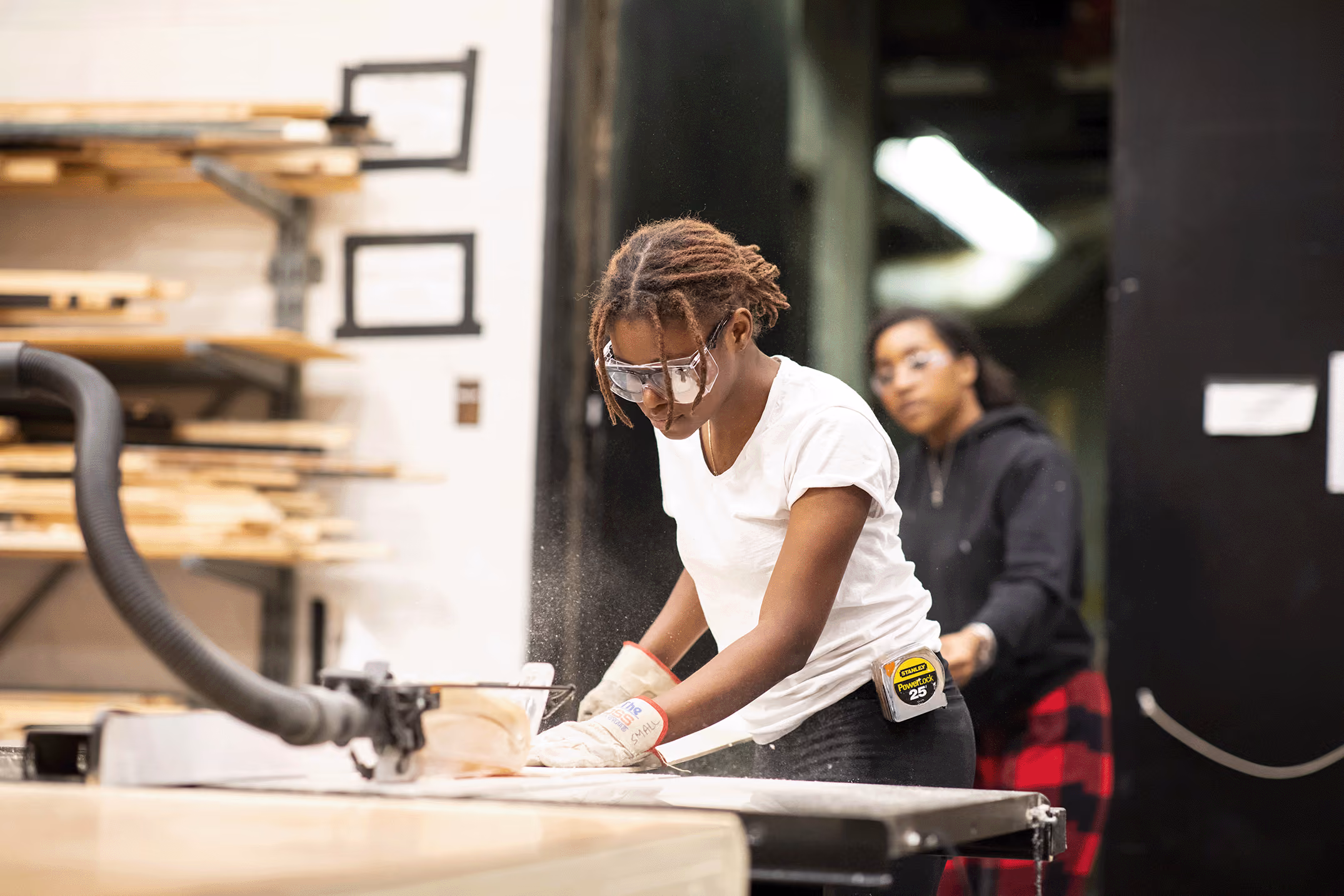 A female student cuts a piece of wood in the scene shop.
