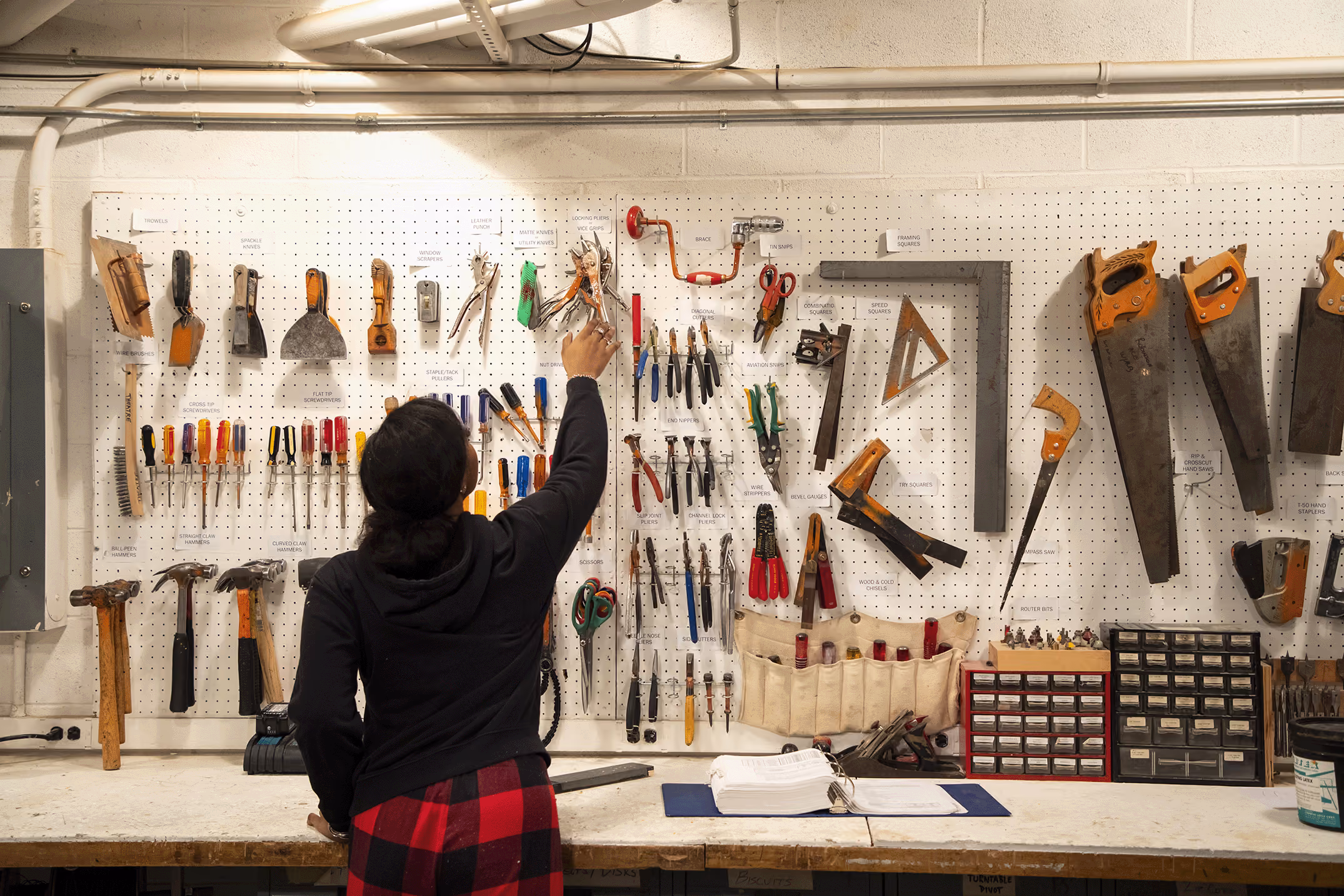 A female student reachers for pliers from a wall of tools in the set design shop.