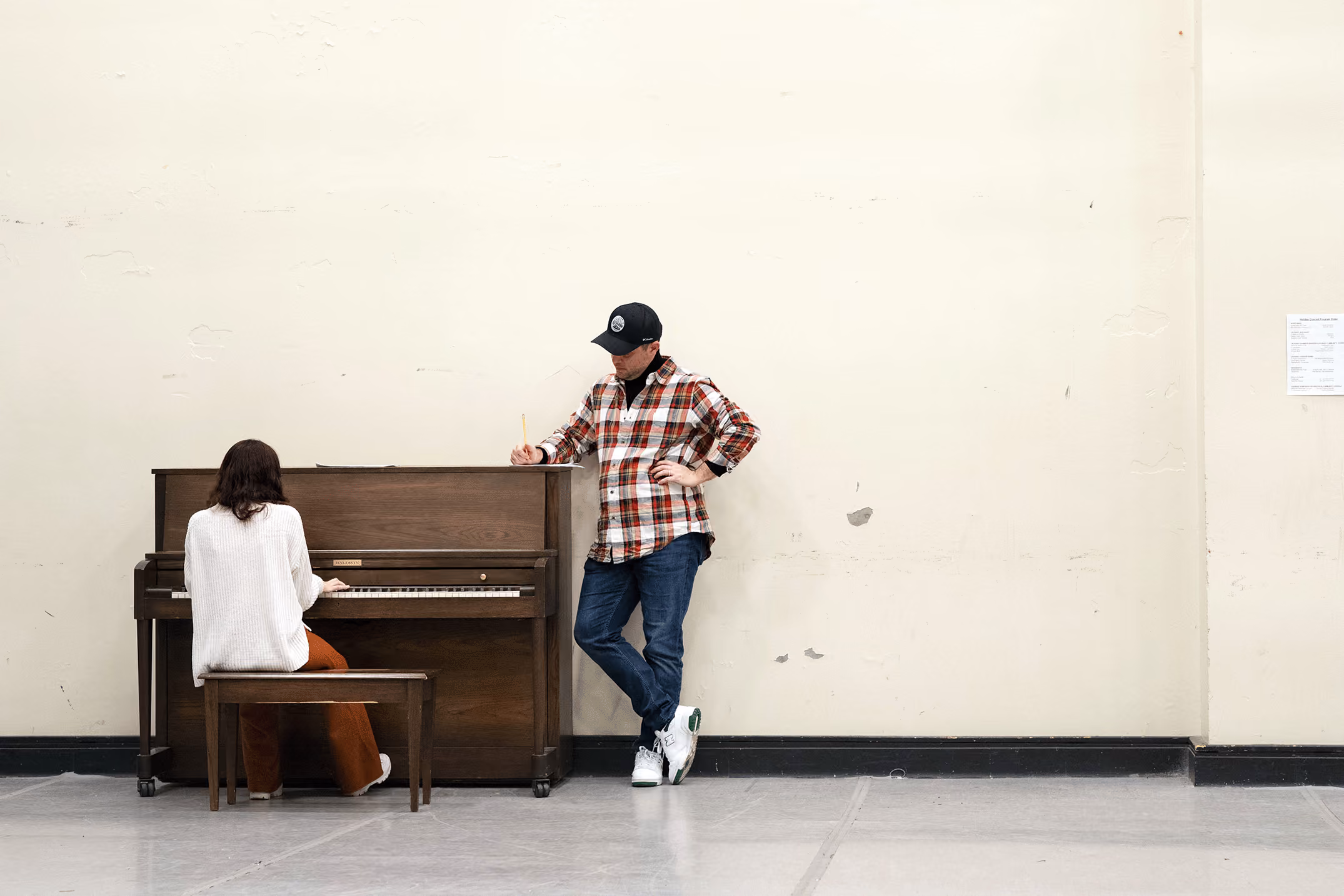 Director Ryan Garbayo makes notes while leaning on an upright piano as a student plays.