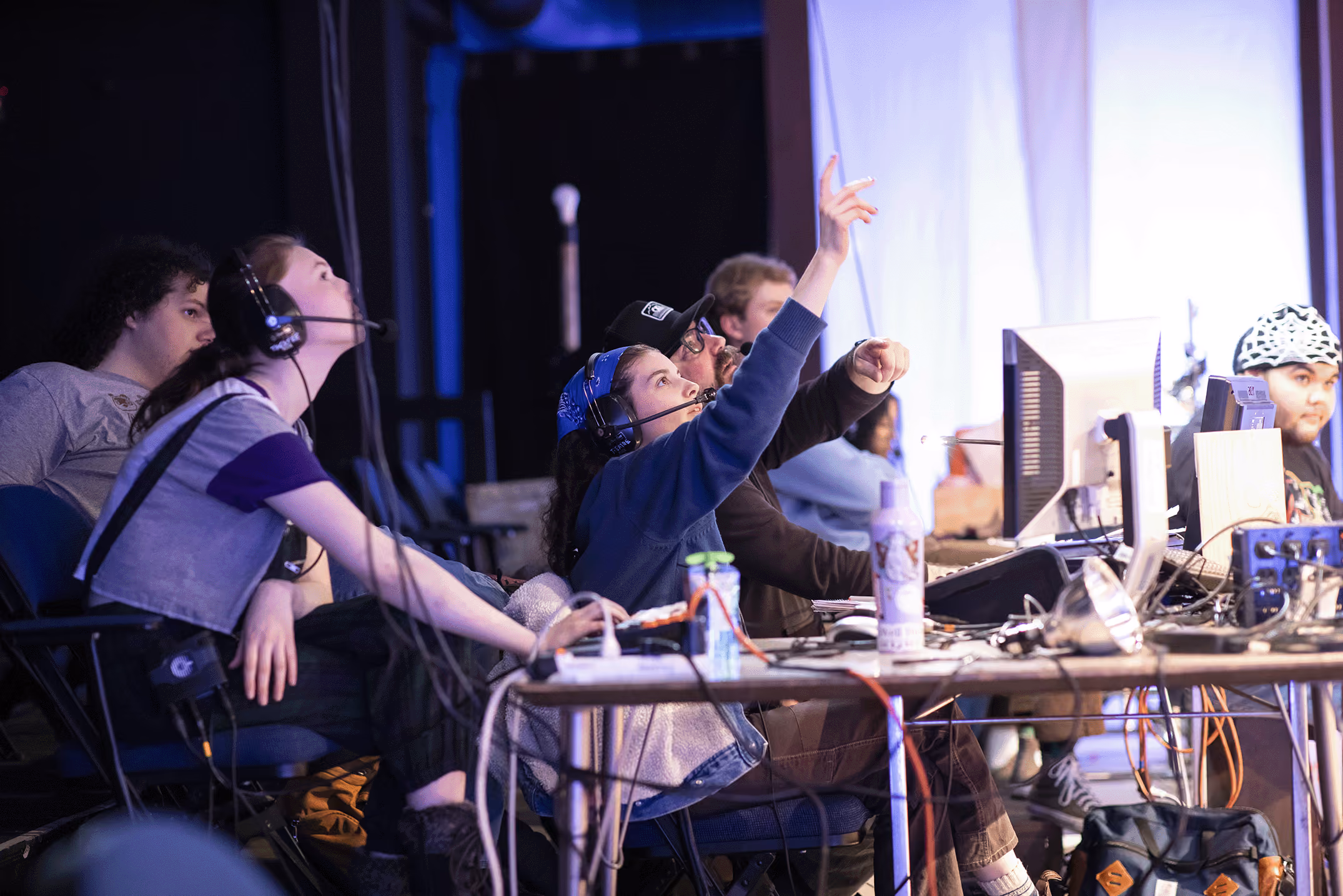 A group of individuals from the technical crew wearing headsets gesture to lights overhead.