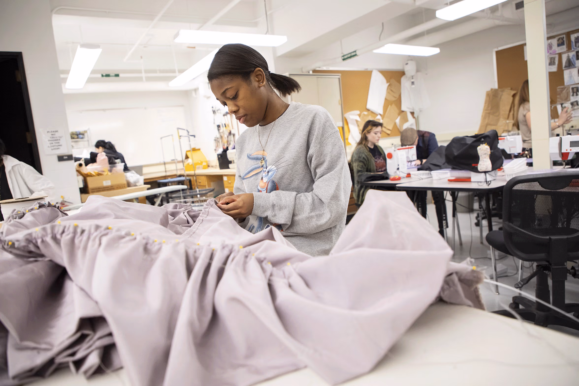 A female student hand sews a large piece of fabric.