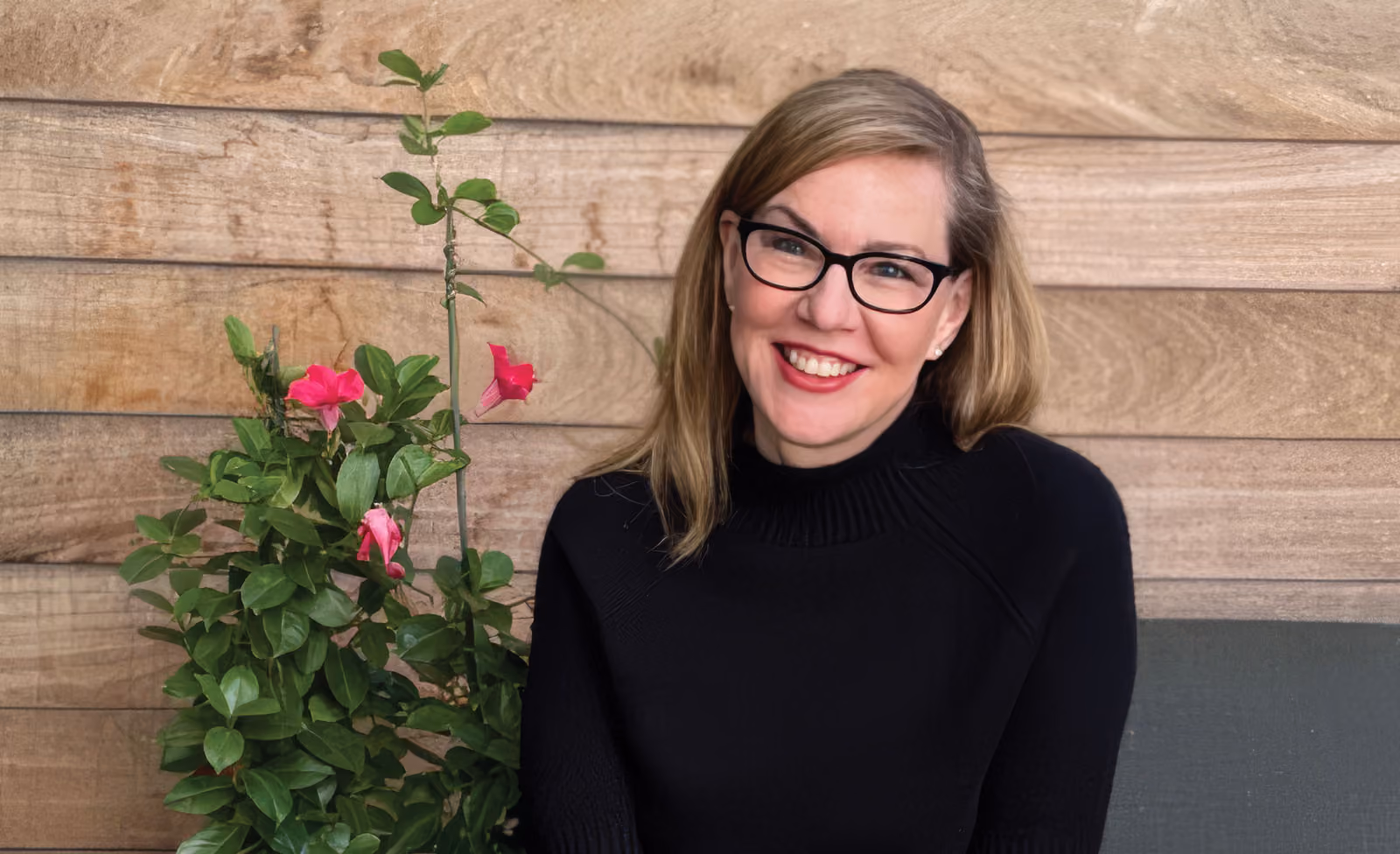 Debbie Millman in front of a rustic wall and flowers.