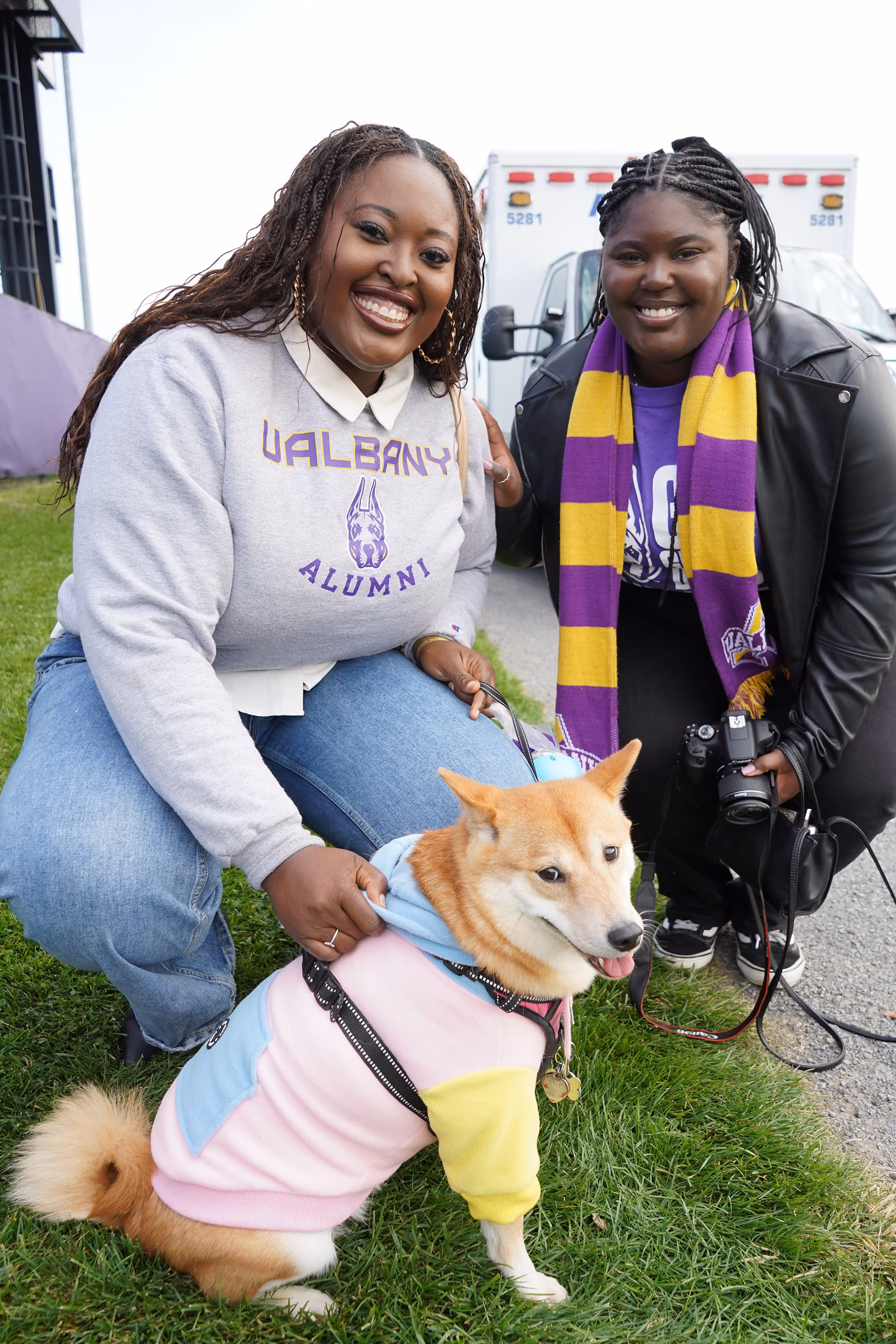 Two people wearing UAlbany shirts pose with a cute dog.