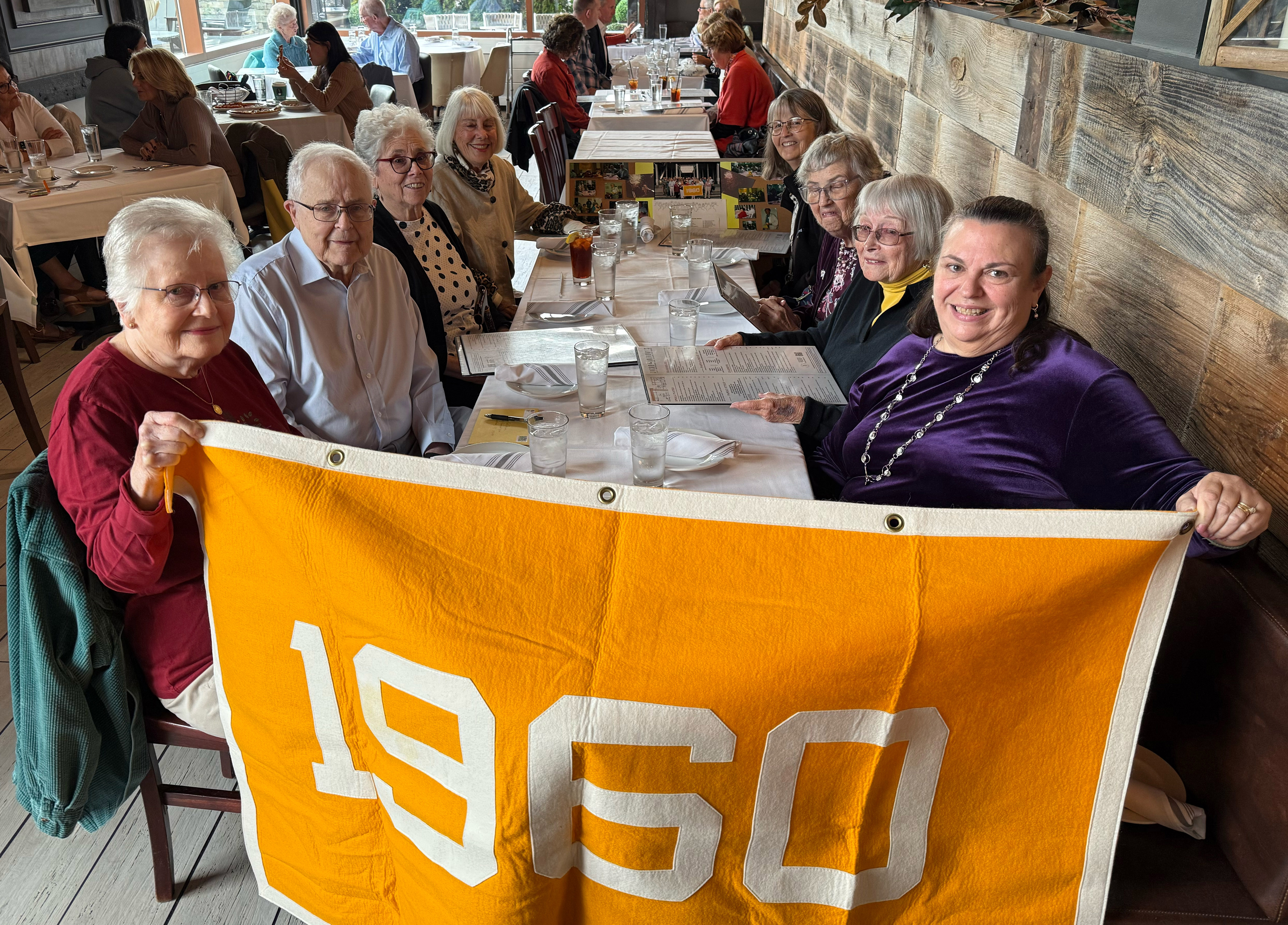 A group of people sit at a table with a banner that reads "1960"