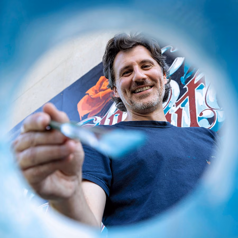Michael Conlin smiles while painting in a blue backdrop.