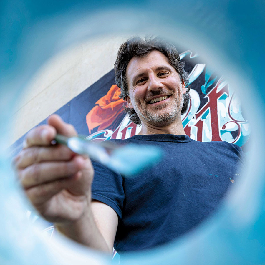 Michael Conlin smiles while painting in a blue backdrop.