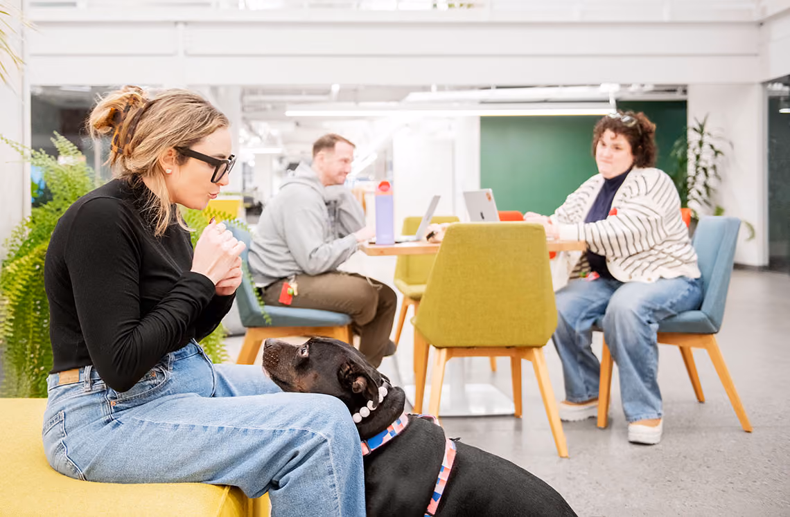 Adele sits with a black dog in a Duolingo common area.