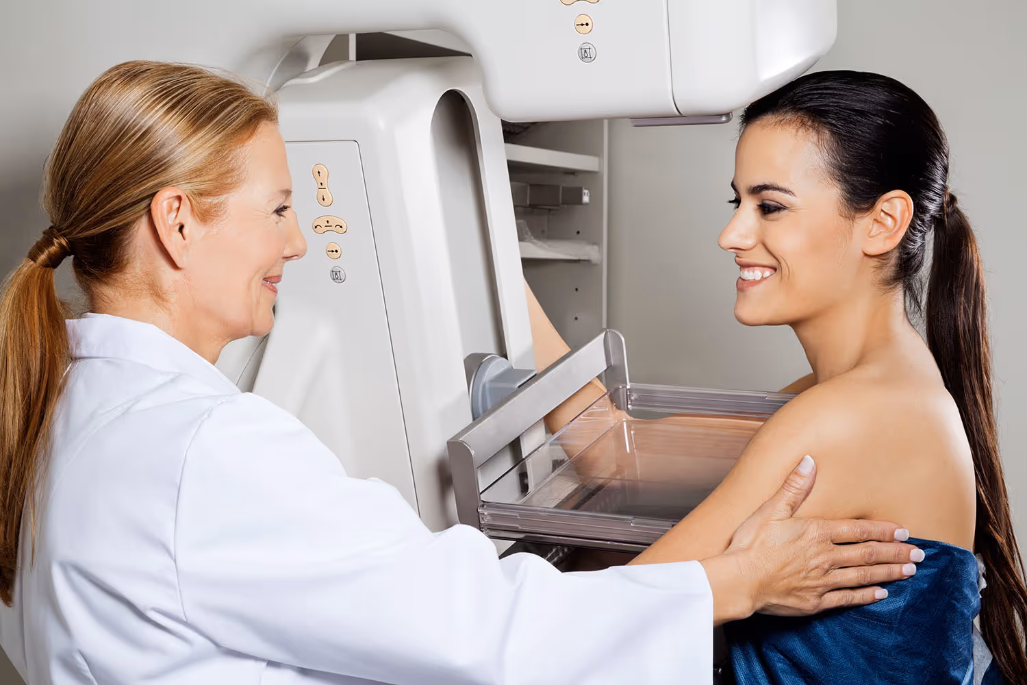 Woman undergoing a mammogram exam with a healthcare professional assisting her.