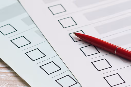 Two sheets of paper with multiple empty checkboxes and a red pen resting on one sheet.