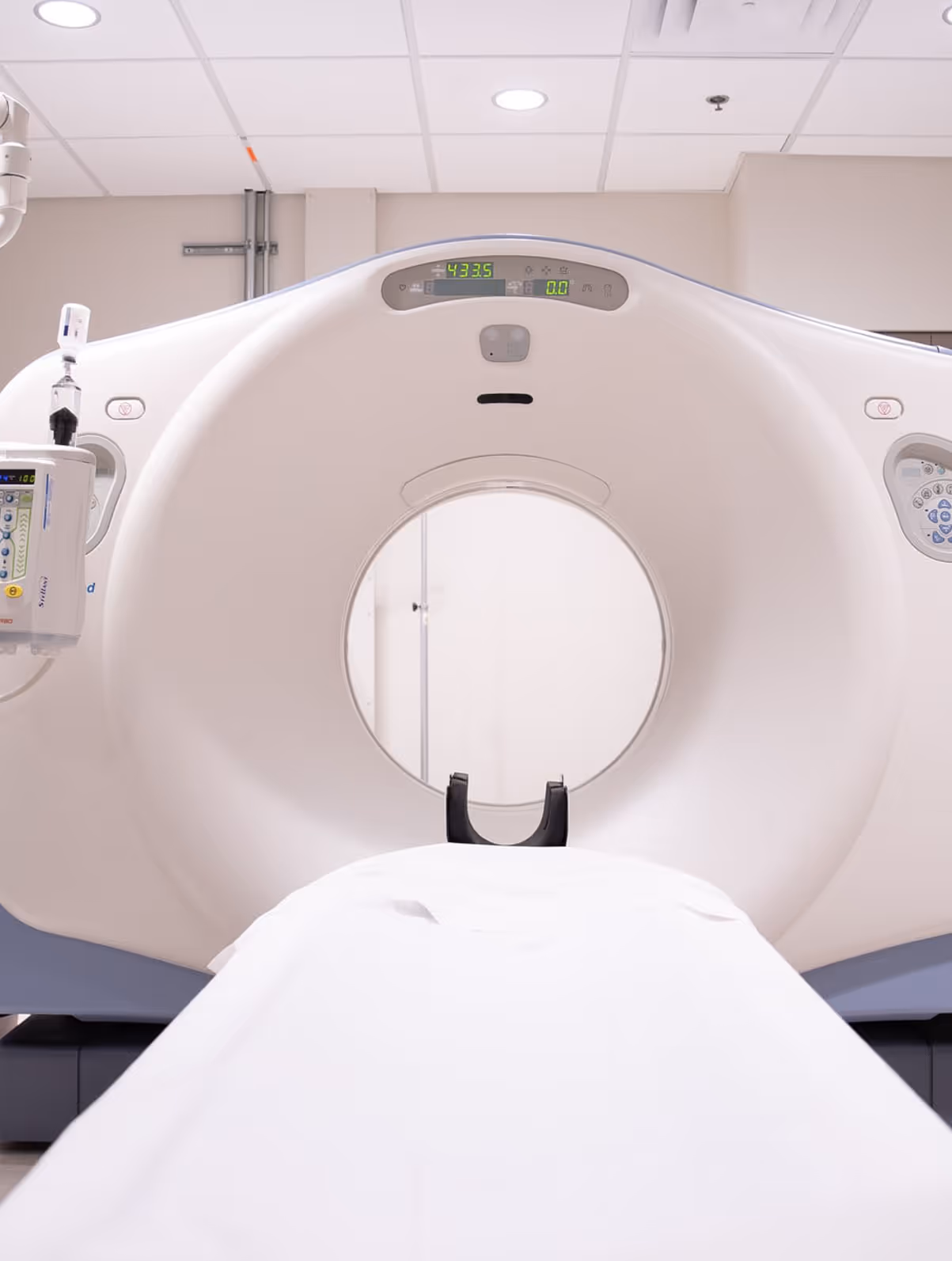 Front view of a modern CT scanner with a patient table covered in white sheets extending into the circular scanner opening.
