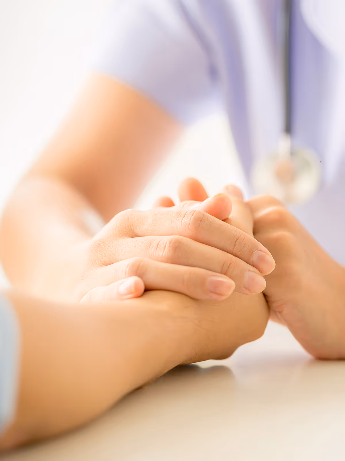 Close-up of a healthcare professional holding a patient's hand in a comforting gesture.