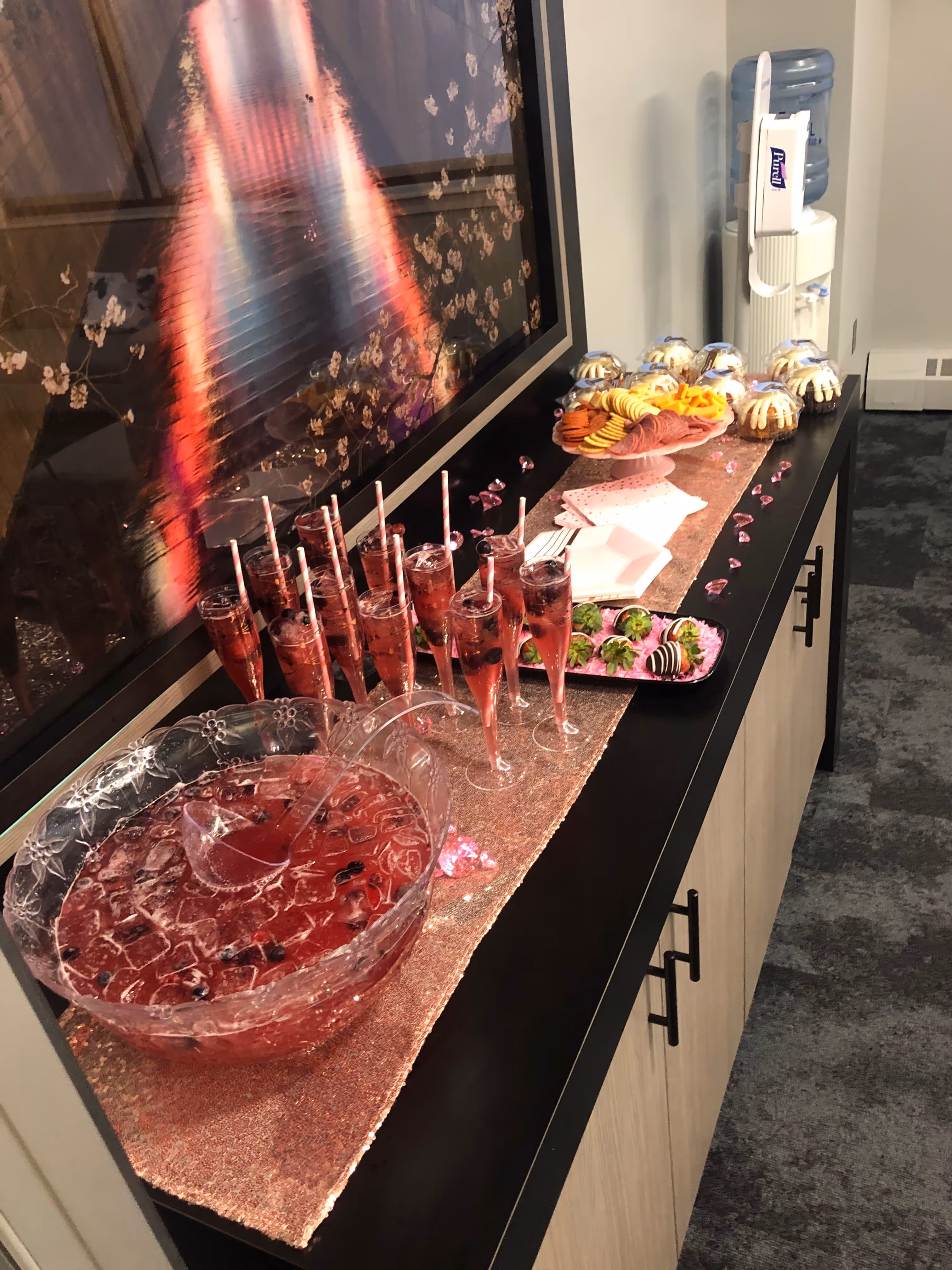 Table with pink punch bowl and glasses, tray of chocolate-covered strawberries, a platter with crackers and meats, and mini bundt cakes.