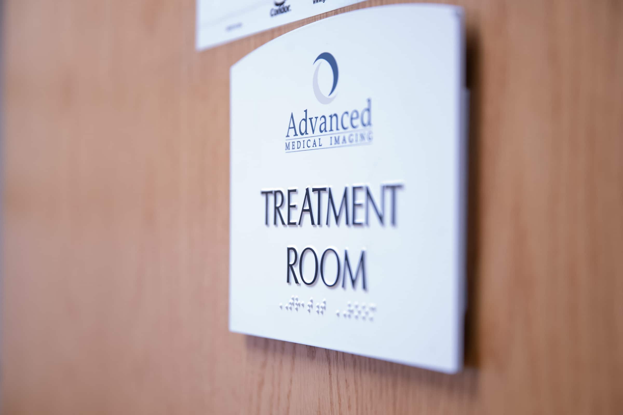 Sign on a wooden door reading Advanced Medical Imaging Treatment Room, with braille text below.