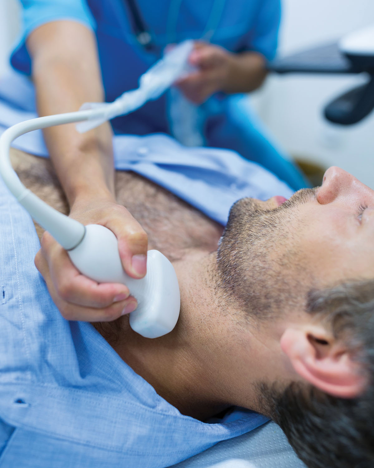 A sonographer performing a neck ultrasound on a patient lying on an exam table.