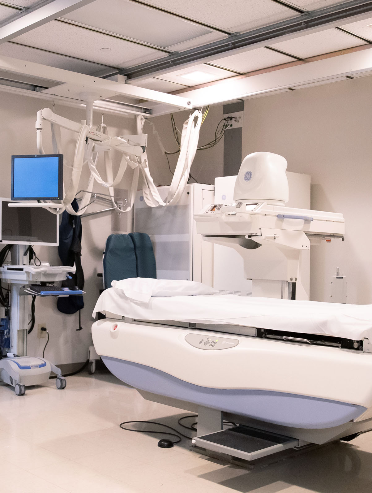 An X-ray examination room with a patient table and an overhead radiography tube.
