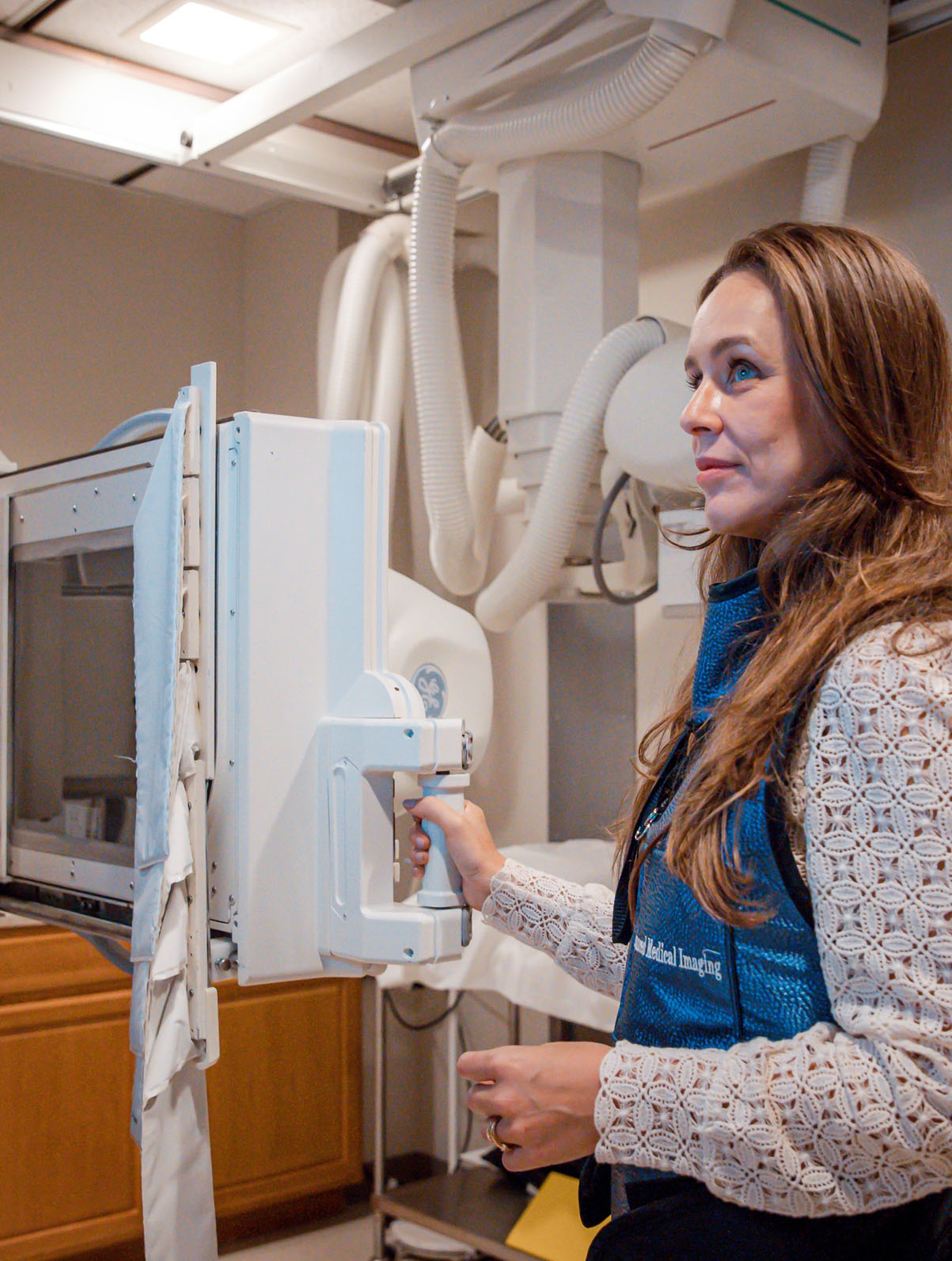 A medical professional wearing a blue protective vest operating an X-ray machine in a clinical room.