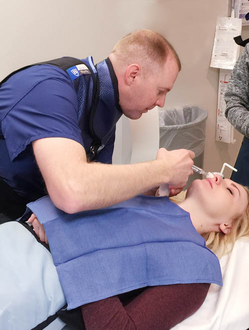 A clinician administering a SphenoCath nasal catheter treatment to a reclined patient.