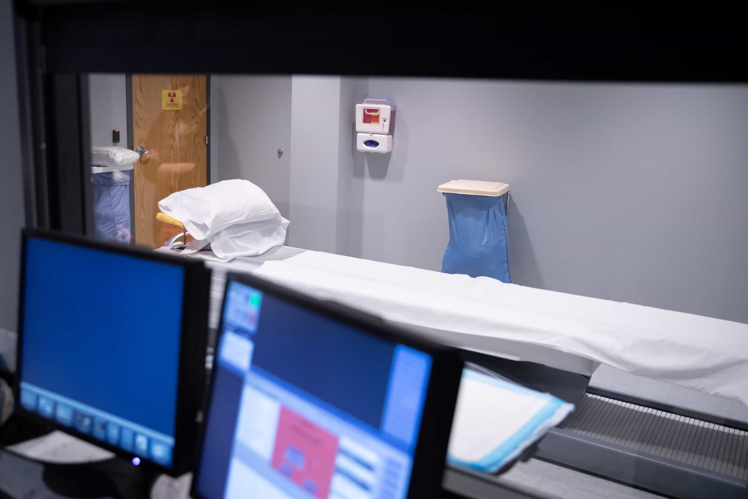 Reading room monitors displaying scan images beside a prepared patient table.