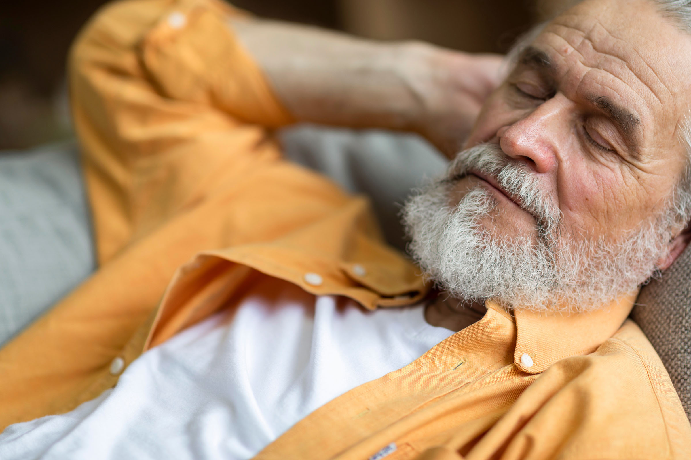 An older man in an orange shirt resting with his eyes closed.