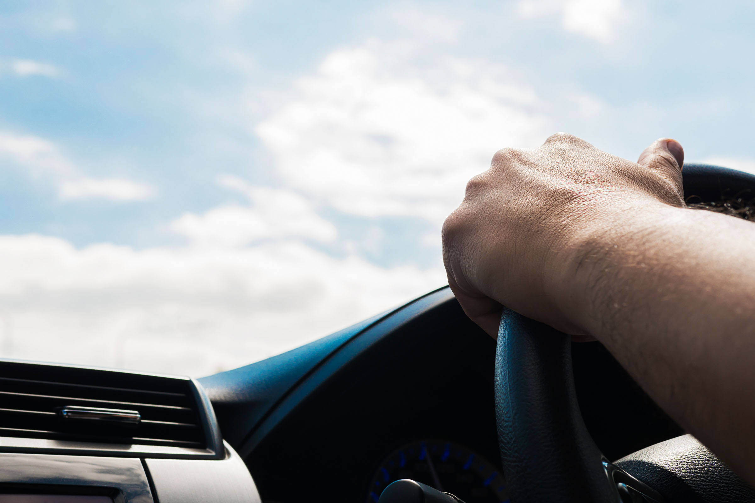 A person's hands on a steering wheel while driving.
