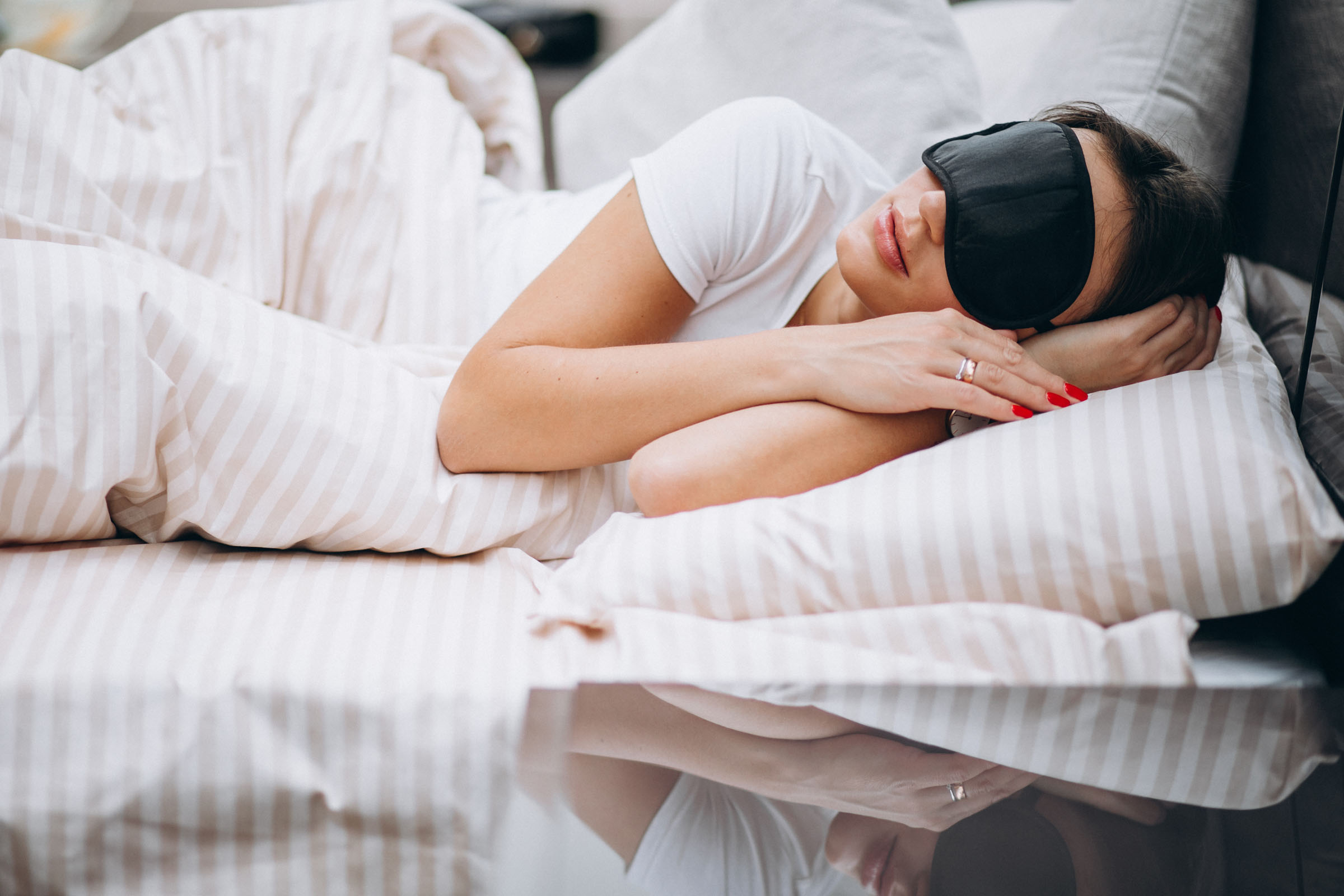 A woman resting in bed with a sleep mask on.