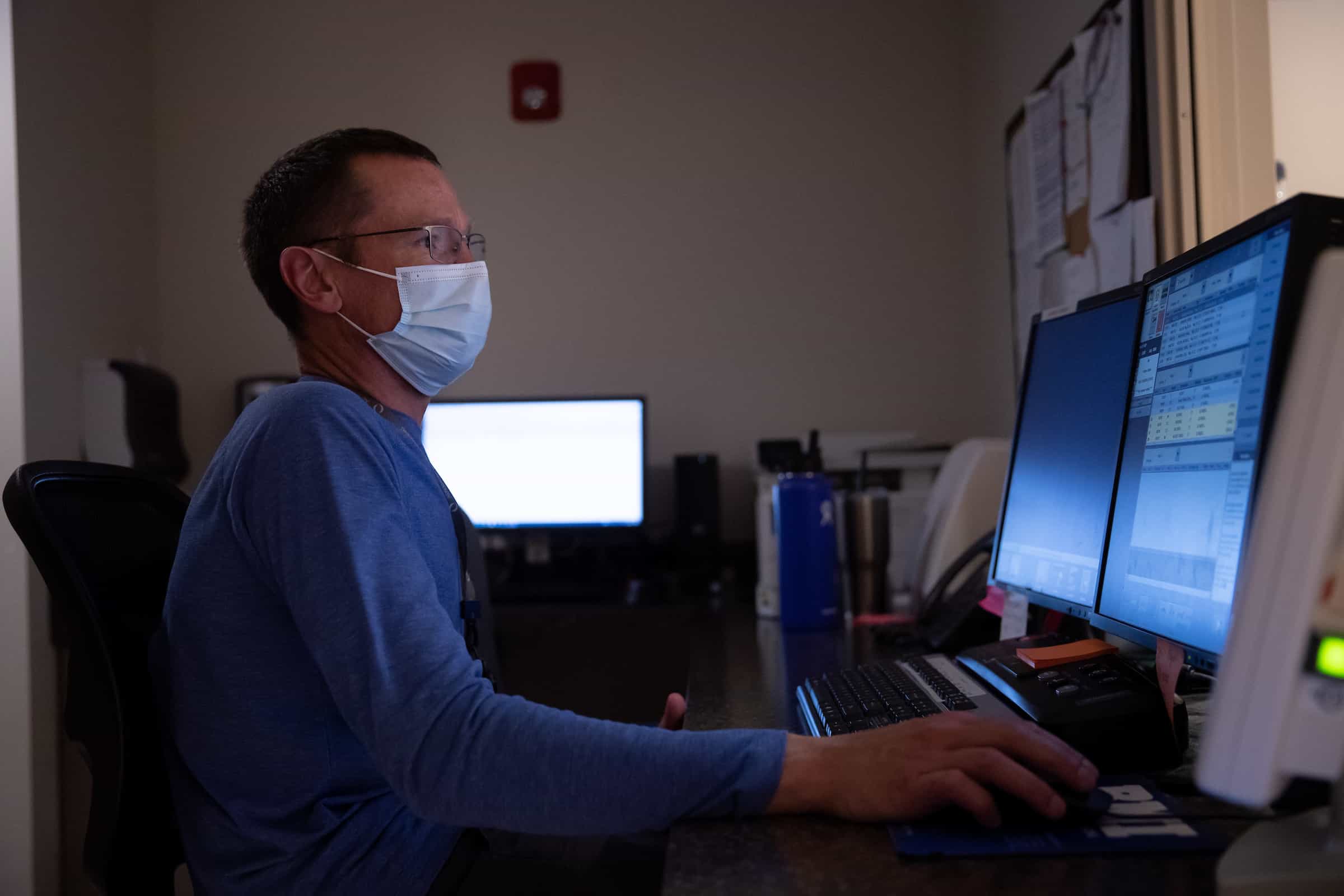 A masked radiologist reviewing images at a multi-screen reading workstation.