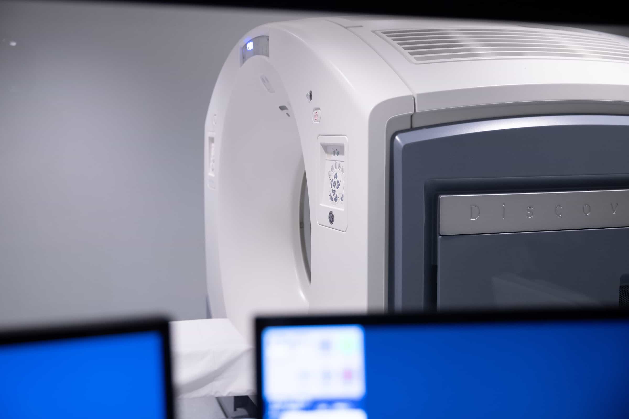 A CT scanner behind a workstation monitor displaying scan images.