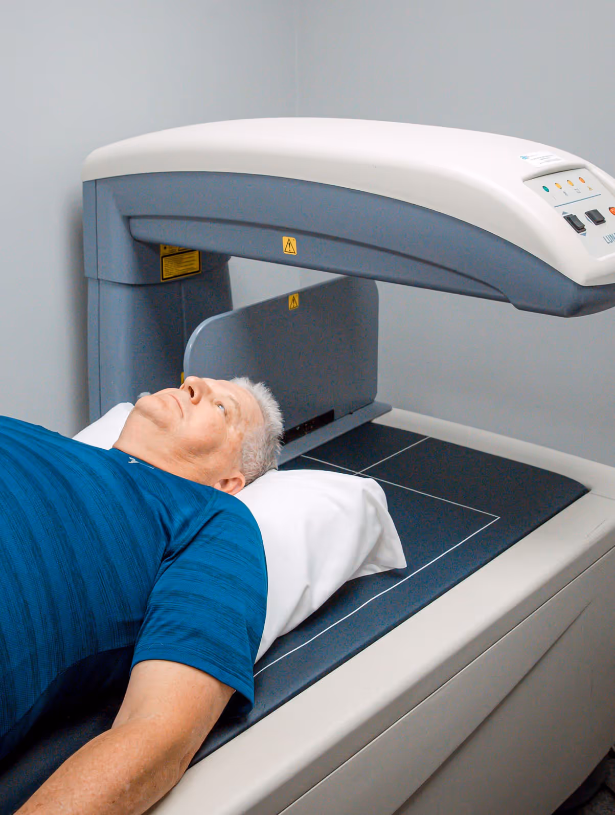 Adult patient in comfortable clothing speaks with a healthcare professional in a modern radiology waiting room, with a tablet showing a subtle bone density scan illustration.