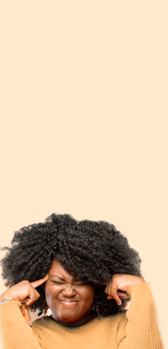 Woman with curly hair wearing a mustard sweater pressing her fingers to her temples with eyes closed and a tense expression.