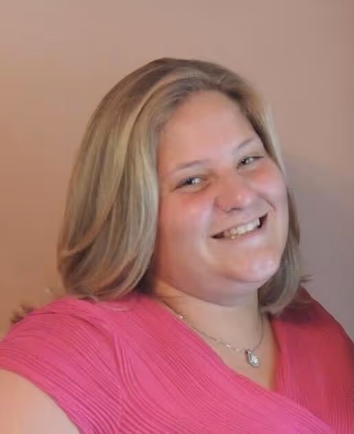 Smiling woman with shoulder-length blonde hair wearing a pink top and a necklace.