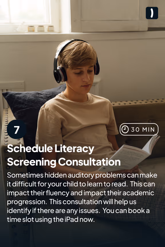 A teenage boy wearing headphones sits on a couch reading a book, illustrating a literacy screening consultation.