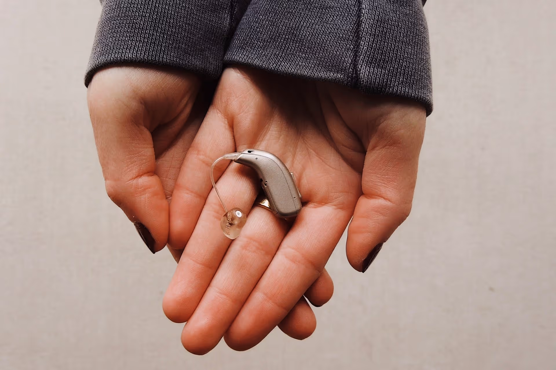 Pair of hands holding a beige hearing aid device with a clear earpiece.