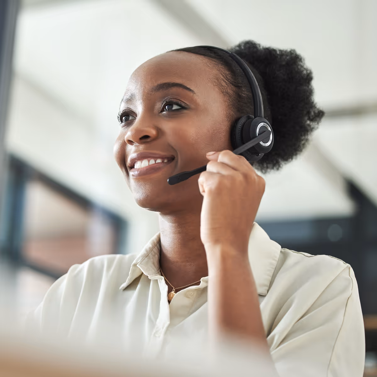 Smiling woman wearing a headset and speaking in a bright office.