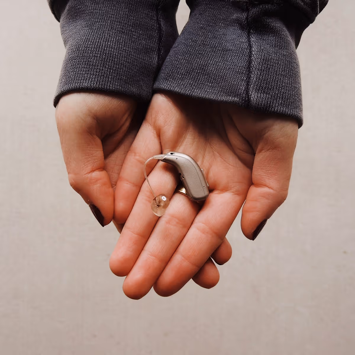 Two hands holding a small, beige behind-the-ear hearing aid device.