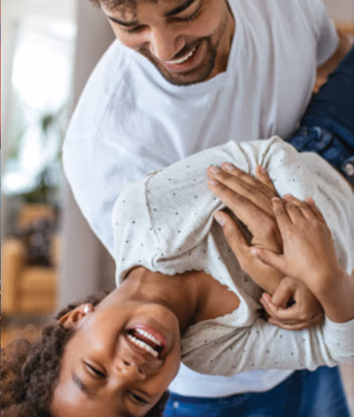 Smiling father holding and playfully lifting his laughing child indoors.