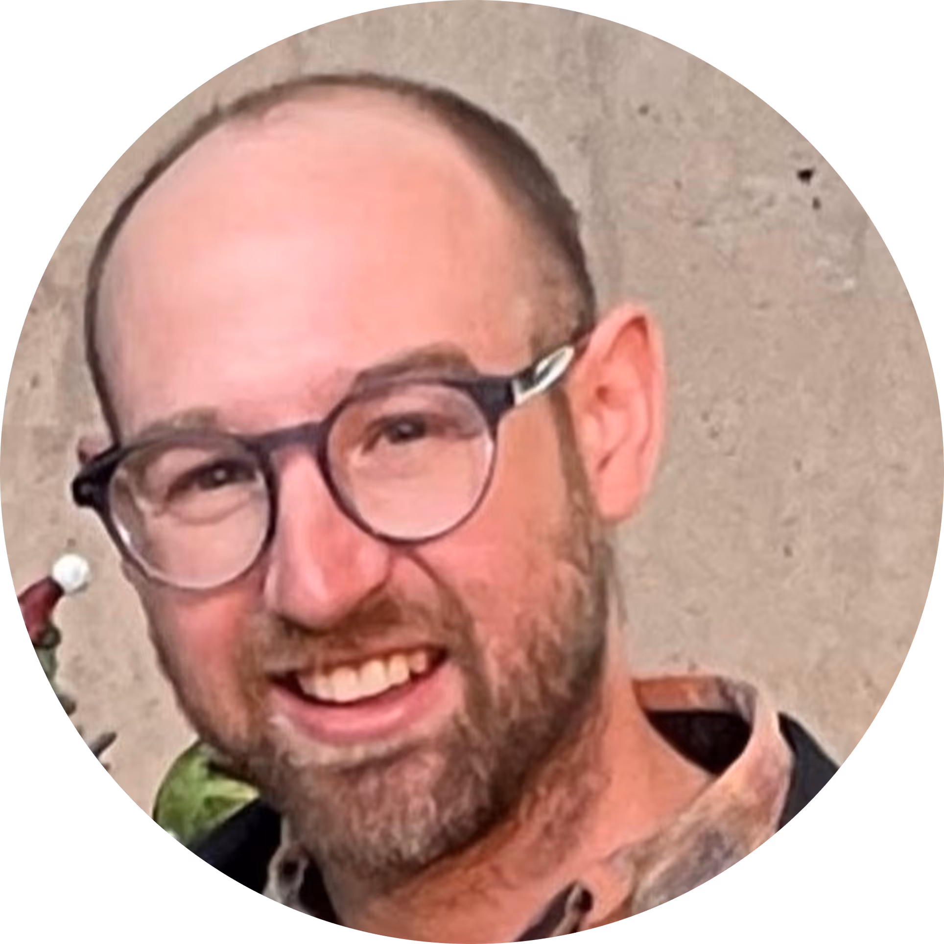 Smiling bald man with glasses and beard wearing a checkered shirt.